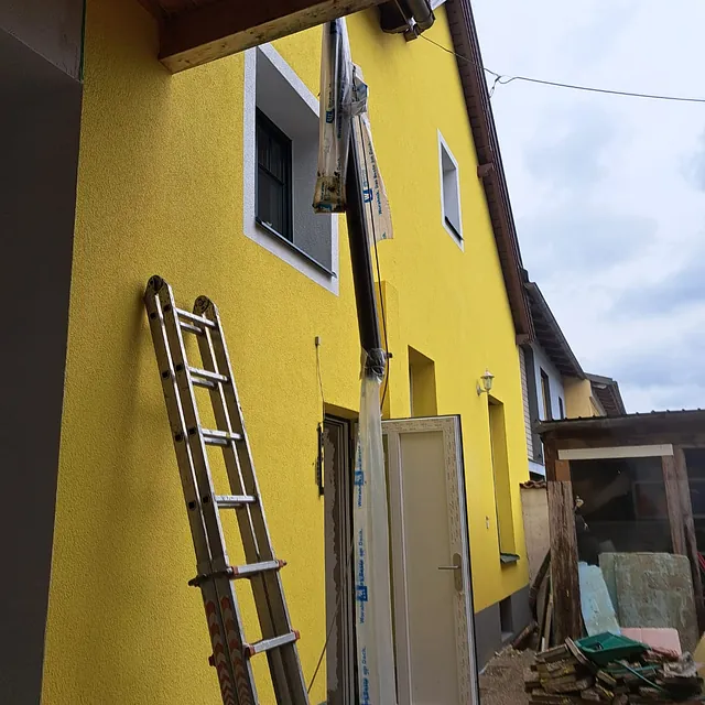 Eine Leiter wird verwendet, um ein gelbes Haus zu erklimmen.