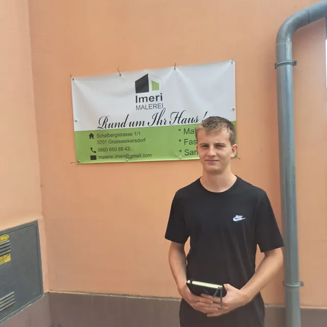 Ein junger Mann steht vor einem Gebäude und hält ein Buch in der Hand.